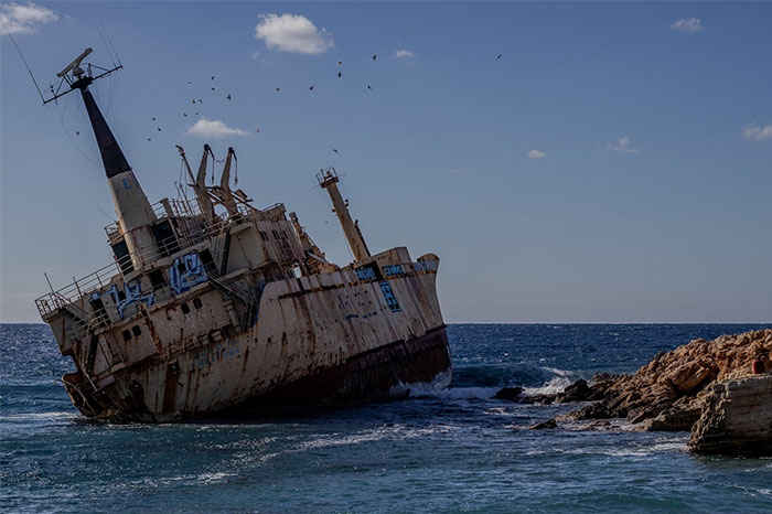 Rusty abandoned shipwreck leaning to one side near rocky shore under a blue sky, representing creepy sea experiences.