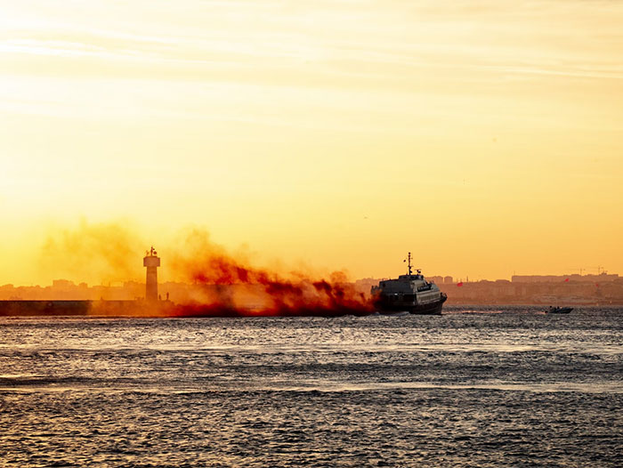 Ship at sea emitting dark smoke near lighthouse at sunset, capturing eerie moments from people who worked at sea.