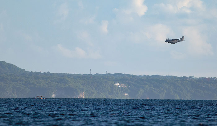 Small boat on sea with distant coastline and a low-flying plane, capturing eerie moments witnessed by people who worked at sea.