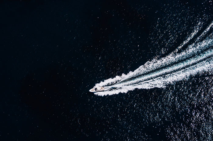 Small boat moving fast on dark sea water with wake trailing behind in a vast open ocean setting, sea workers at sea.