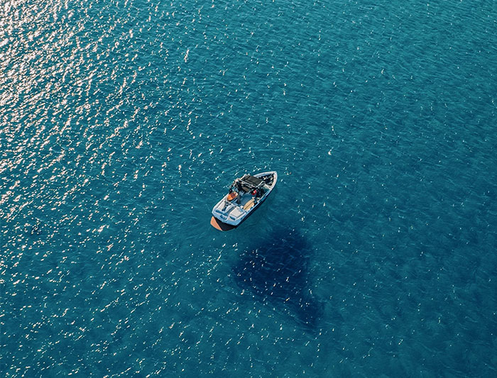 Small boat floating on calm blue ocean with large dark shadow beneath, capturing the eerie side of working at sea.