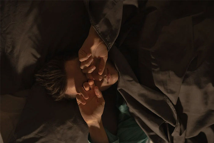 Person resting in bed with hands over face, illustrating the eerie experiences shared by people who worked at sea.