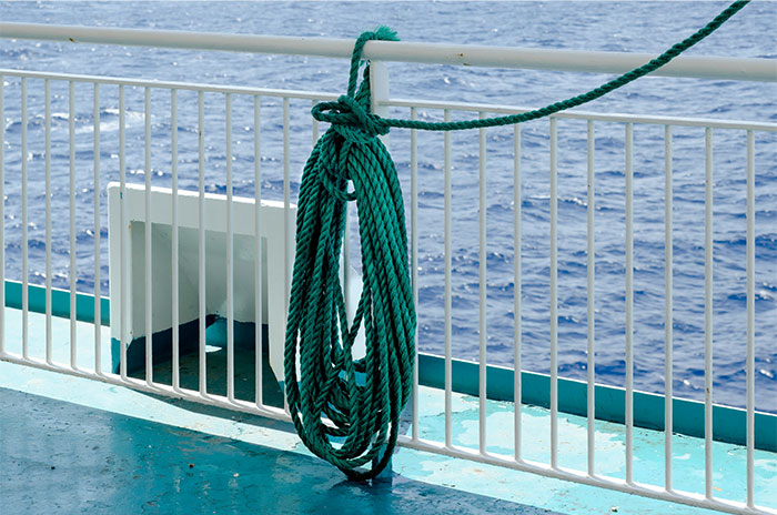 Thick green rope tied on ship railing with ocean view in the background, representing people who worked at sea.