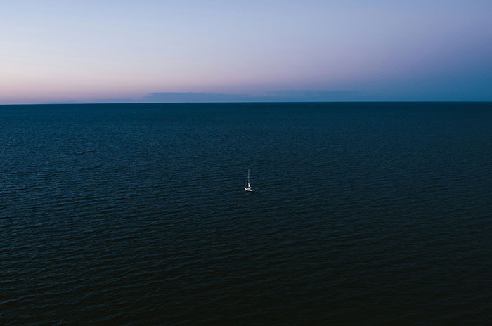 Small sailboat alone on vast dark sea at dusk, representing creepy experiences people shared while working at sea.