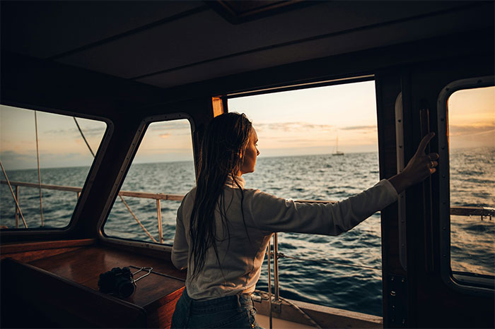 Woman working at sea on a boat, looking out over the ocean during sunset, capturing eerie maritime experiences.