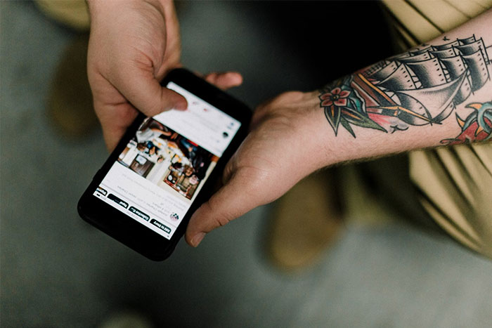 Person with a ship tattoo on arm holding a smartphone showing stories from people who worked at sea about creepy experiences.