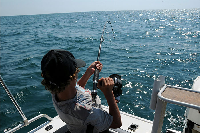 Person fishing from a boat on a sunny day at sea, illustrating experiences shared by people who worked at sea.