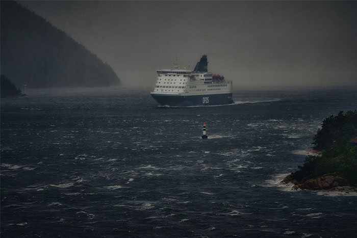 Large ferry sailing through dark, stormy sea with foggy coastline, illustrating creepy experiences at sea.