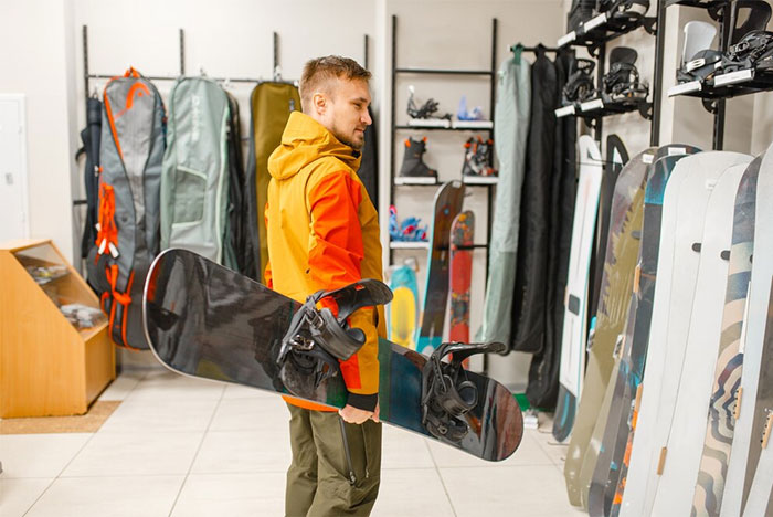 A man explores an ultra wealthy snowboard collection, holding a snowboard in a store filled with luxury sports gear.