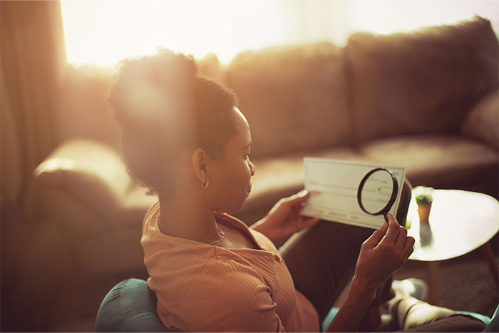 Woman examining a check with a magnifying glass in a cozy living room, representing a glimpse into the ultra wealthy world.
