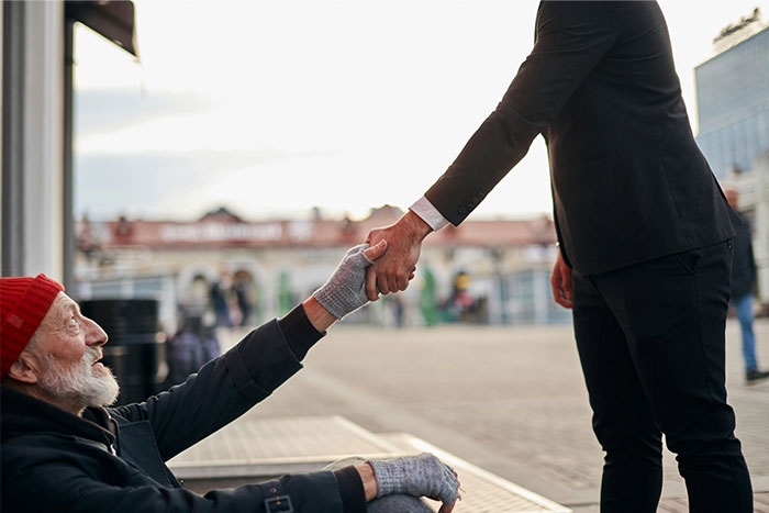 Man in suit offering a handshake to a homeless man, showing a rare glimpse into the world of the ultra wealthy.