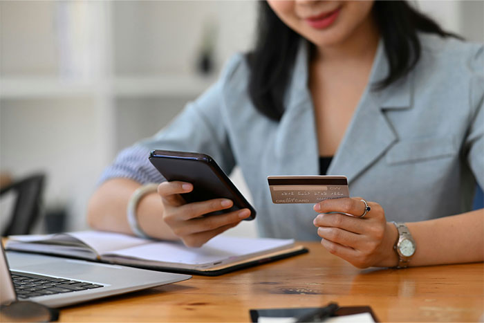 Woman using smartphone and credit card at a desk, offering a glimpse into the world of the ultra wealthy.