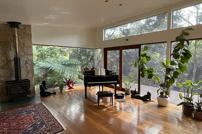 Spacious living room with grand piano, large windows, and plants offering a glimpse into the world of the ultra wealthy.