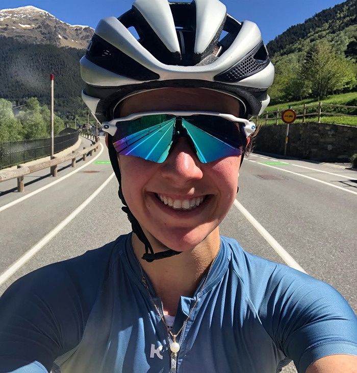 Cyclist wearing helmet and reflective sunglasses smiling on a sunny road, related to fatal crash apology to late Olympian wife.