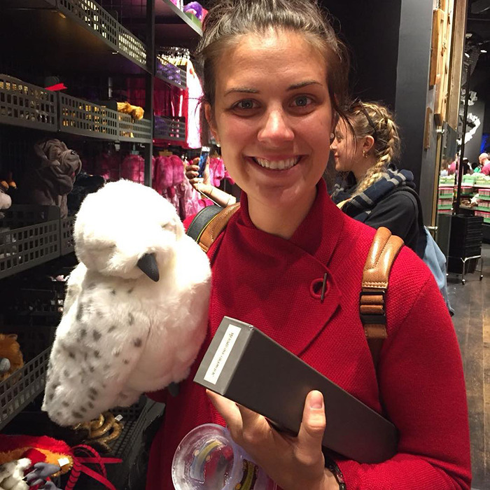Smiling woman in red holding a soft owl toy and a box, related to cyclist apology for fatal crash involving late Olympian wife.
