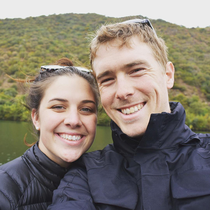Smiling couple outdoors near water with green hills, related to cyclist apology after fatal crash involving Olympian wife.