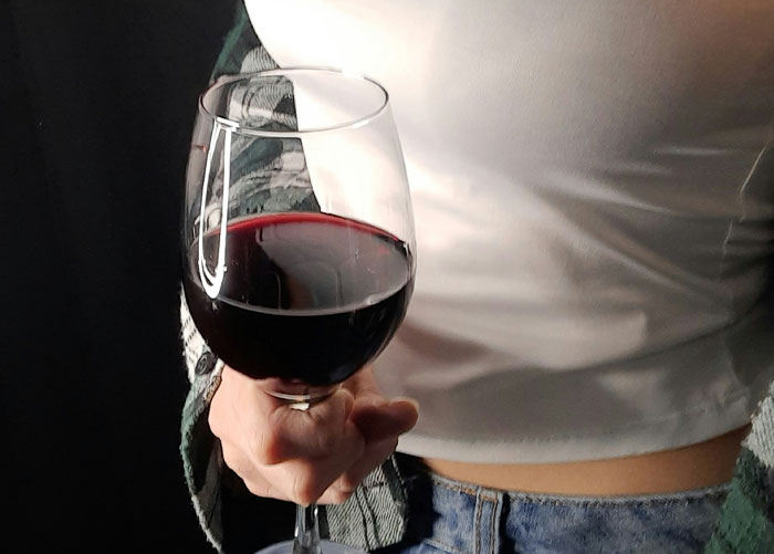 Person holding a glass of red wine highlighting the worst gifts they've ever received in a casual setting.