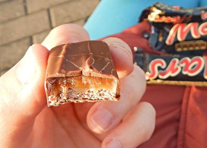 Hand holding a partially eaten Mars chocolate bar, illustrating one of the worst gifts people have received.