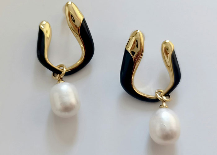 Pair of gold and black snake-shaped earrings with dangling white pearls, representing one of the worst gifts received.