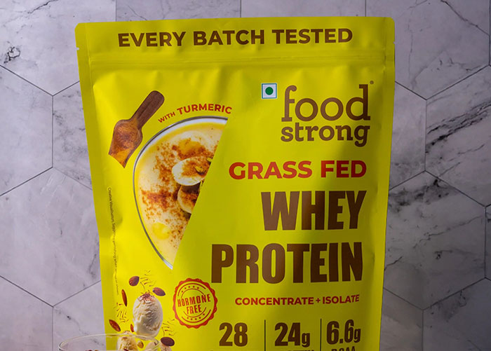 Bright yellow package of grass fed whey protein with turmeric, highlighting tested quality and high protein content.