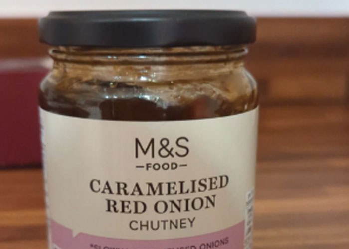 Jar of caramelised red onion chutney on a wooden surface, representing one of the worst gifts received by people.