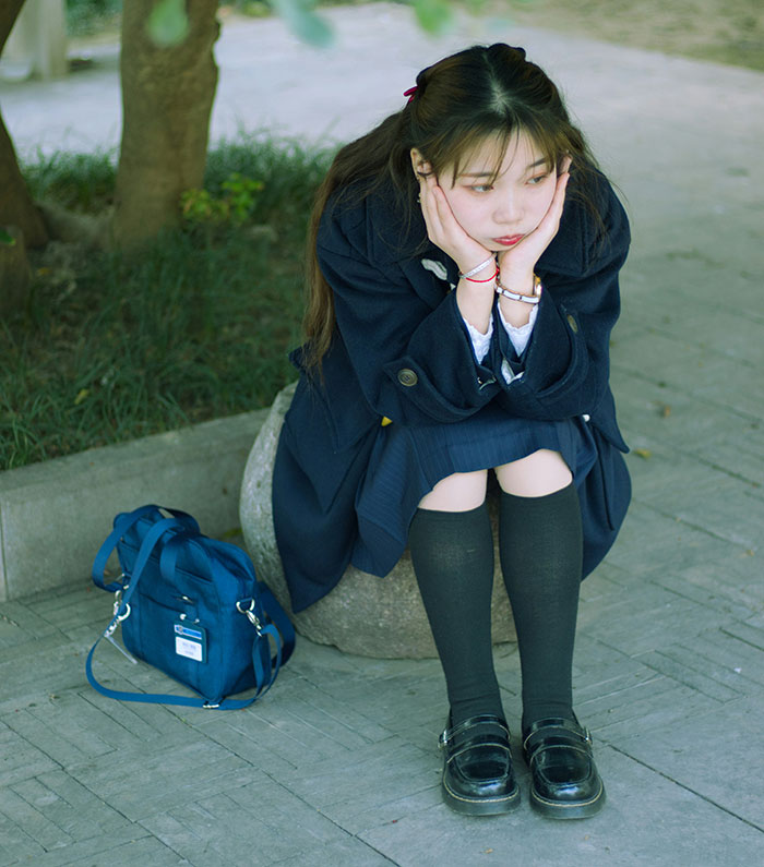 Teen girl sitting alone outdoors looking pensive, illustrating the impact of helicopter parenting on children’s emotions.