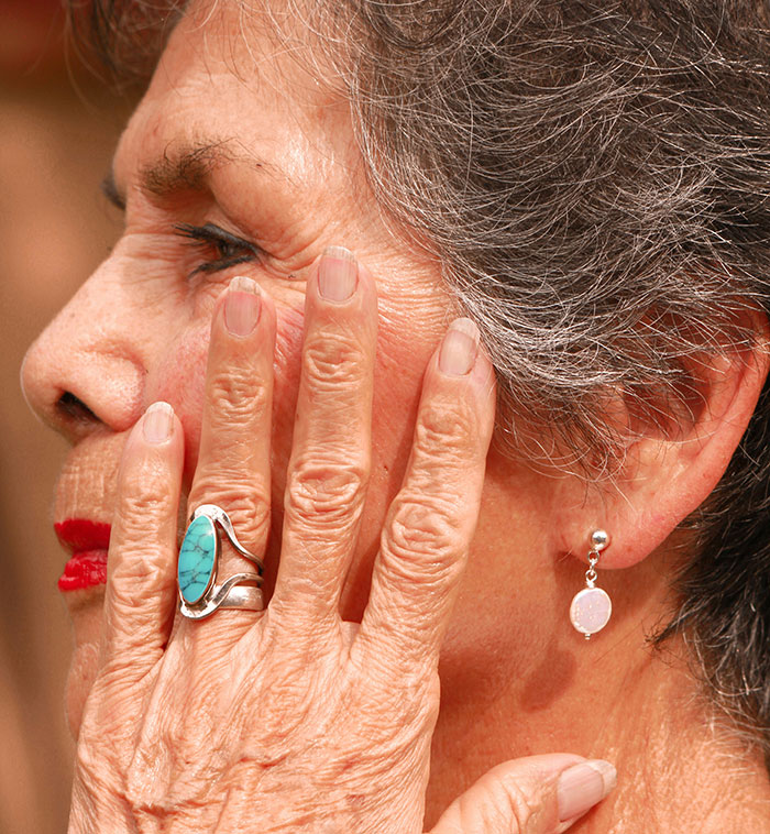 Close-up of an elderly woman wearing a turquoise ring and earrings showing signs of aging and worry, illustrating helicopter parenting.