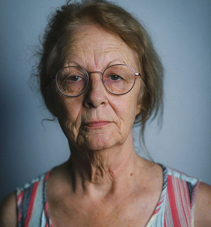Elderly woman with glasses and serious expression, representing intense helicopter parenting emotions in a close-up portrait.
