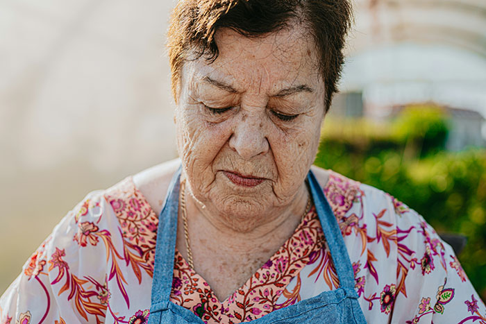 Elderly woman wearing a floral shirt and denim apron focused on an activity, illustrating helicopter parenting intensity.