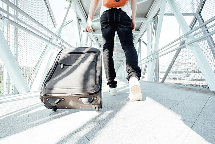 Person walking on a metal bridge pulling luggage, illustrating helicopter parenting in travel and supervision situations.