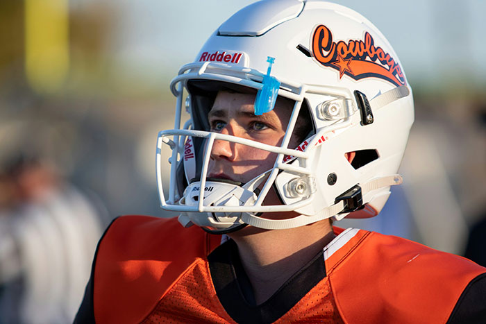 Young football player in orange gear and white helmet, representing the impact of helicopter parenting on children's activities.