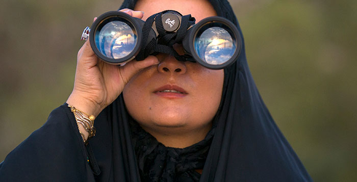 Woman in dark clothing holding binoculars, symbolizing helicopter parenting surveillance and intense child monitoring.