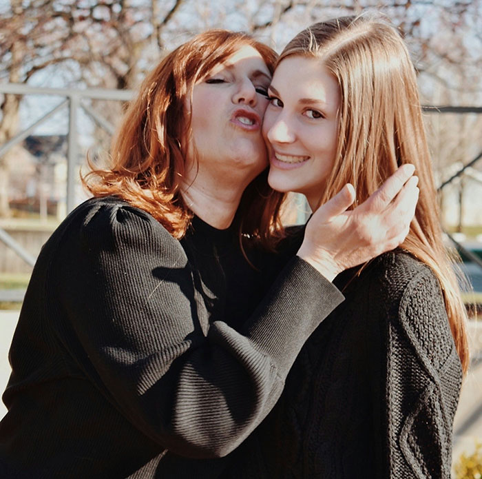 Mother displaying helicopter parenting by hugging and holding her teenage daughter closely outdoors on a sunny day.