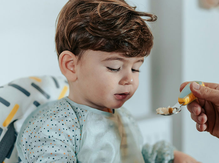 Toddler being fed by a parent, illustrating helicopter parenting with close supervision during mealtime.
