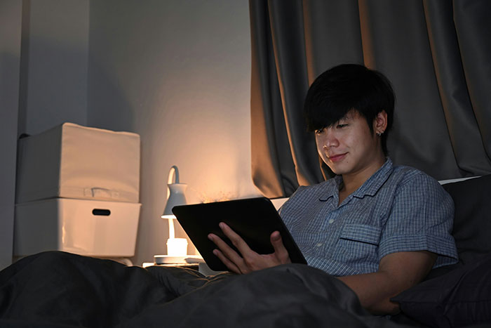 Young person in pajamas using a tablet in bed at night, illustrating the effects of helicopter parenting on screen time.