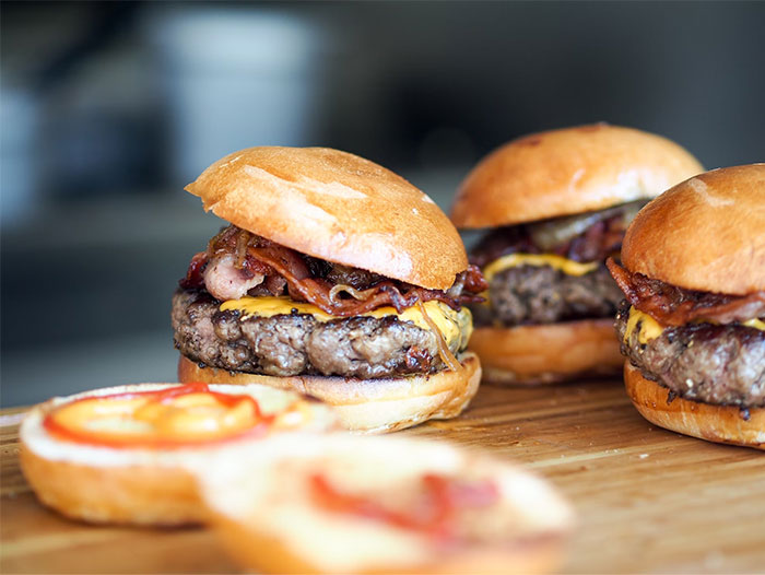 Close-up of bacon cheeseburgers on a wooden board representing chaotic food choices witnessed at a wedding event.