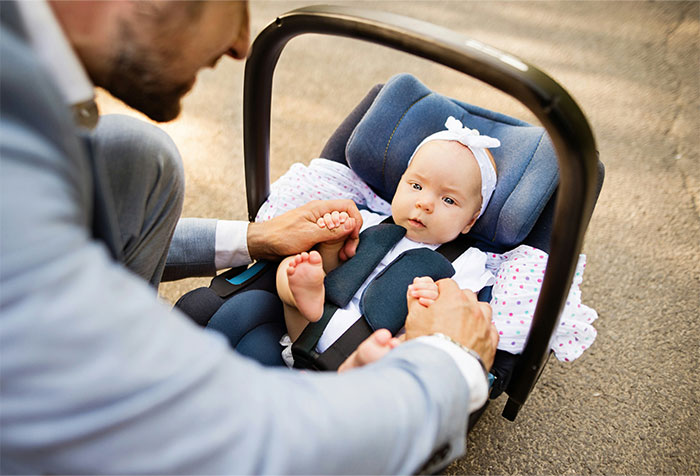 Man holding baby in car seat at outdoor wedding, capturing a chaotic moment witnessed at a wedding celebration.