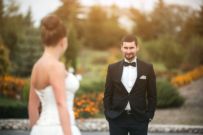 Groom in a tuxedo looking at bride in wedding dress outdoors, capturing chaotic wedding moments witnessed by guests.