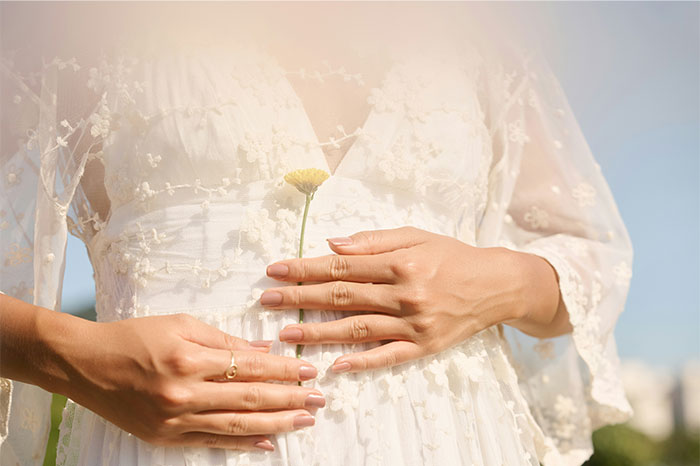 Close-up of a bride in a white lace dress holding a small yellow flower, capturing a calm wedding moment amid chaos.