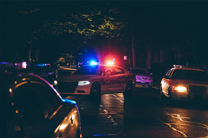 Police cars with flashing lights blocking a dark street at night, hinting at chaotic scenes witnessed at a wedding.