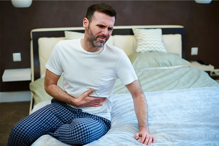 Man in pajamas sitting on bed, clutching stomach in pain, illustrating chaotic moments witnessed at a wedding.