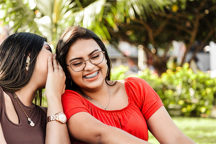 Two women sharing a secret outdoors, smiling and enjoying a moment, capturing chaotic moments witnessed at weddings.