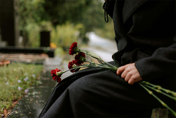 Person in dark clothing holding red flowers while sitting outdoors, symbolizing emotional moments at chaotic weddings witnessed by people.