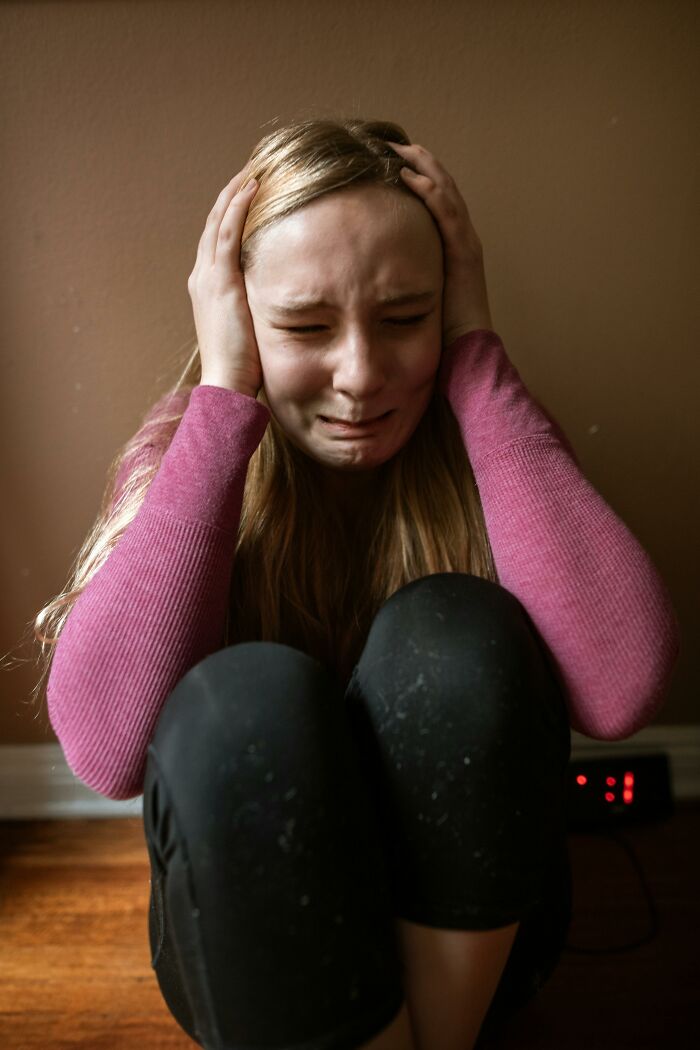 Teenager sitting on floor crying and covering ears, illustrating hurtful things moms said to their children moments.
