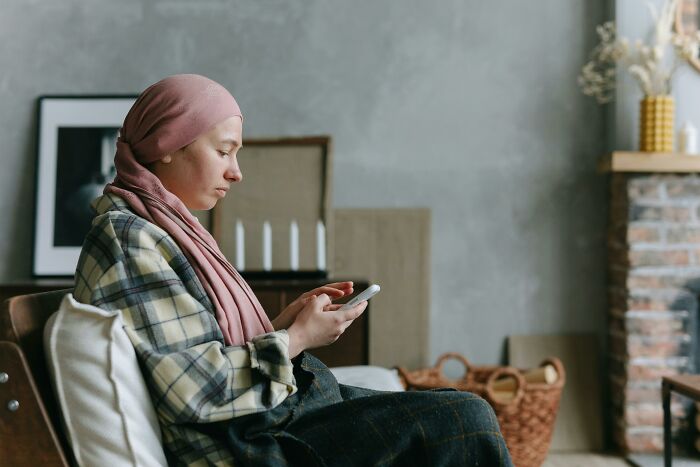 A woman wearing a headscarf sitting on a couch, looking thoughtfully at her smartphone, reflecting on hurtful mom comments.