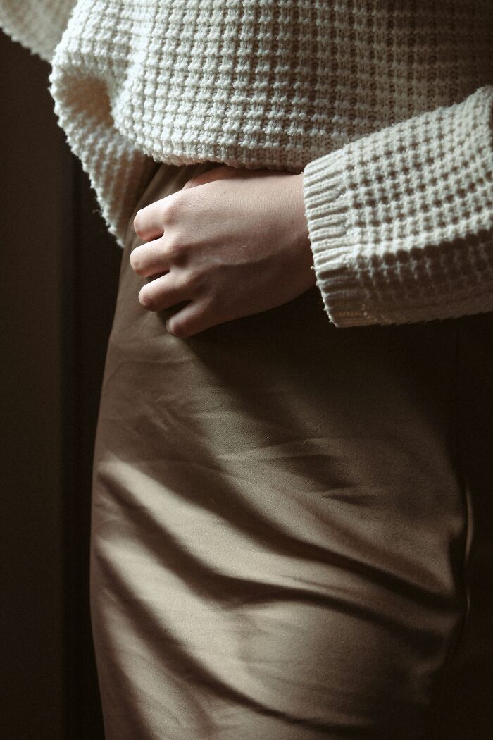 Person wearing a textured white sweater and beige skirt, clutching their midsection, reflecting on hurtful things moms ever said.