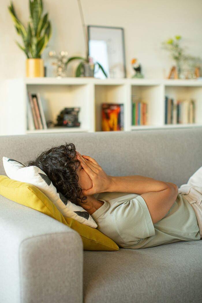 Person lying on a couch with hands covering face, reflecting pain from hurtful things their mom said to them.