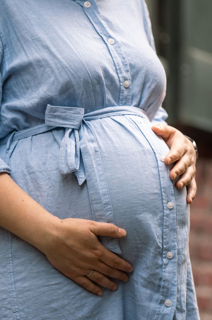 Close-up of a pregnant woman in a blue dress holding her belly, relating to people revealing hurtful things their moms said.