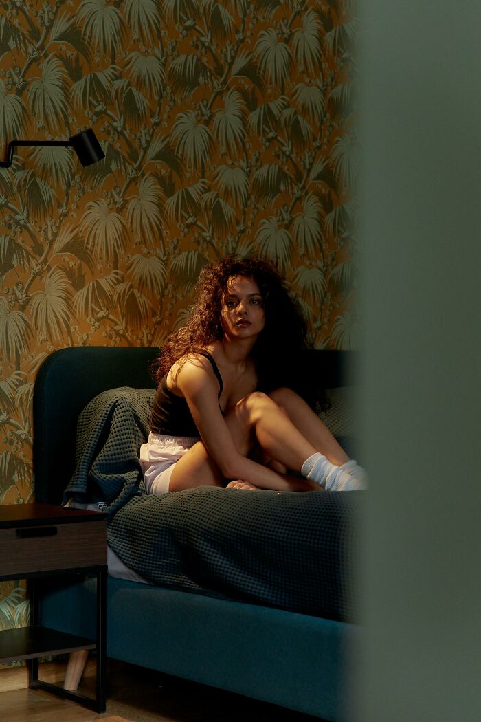 Young woman sitting on a bed looking pensive, illustrating emotional impact of hurtful things moms said to them.