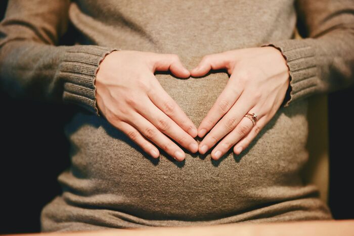 Pregnant woman in a cozy sweater forming a heart shape on her belly, symbolizing motherhood and emotional moments.